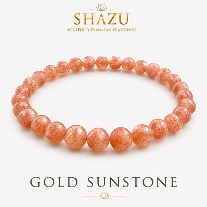 May include: A circular beaded bracelet made of polished, translucent orange-gold sunstone spheres. The text SHAZU SOULFULLY FROM SAN FRANCISCO appears above the bracelet, and the text GOLD SUNSTONE is printed below the jewelry item.