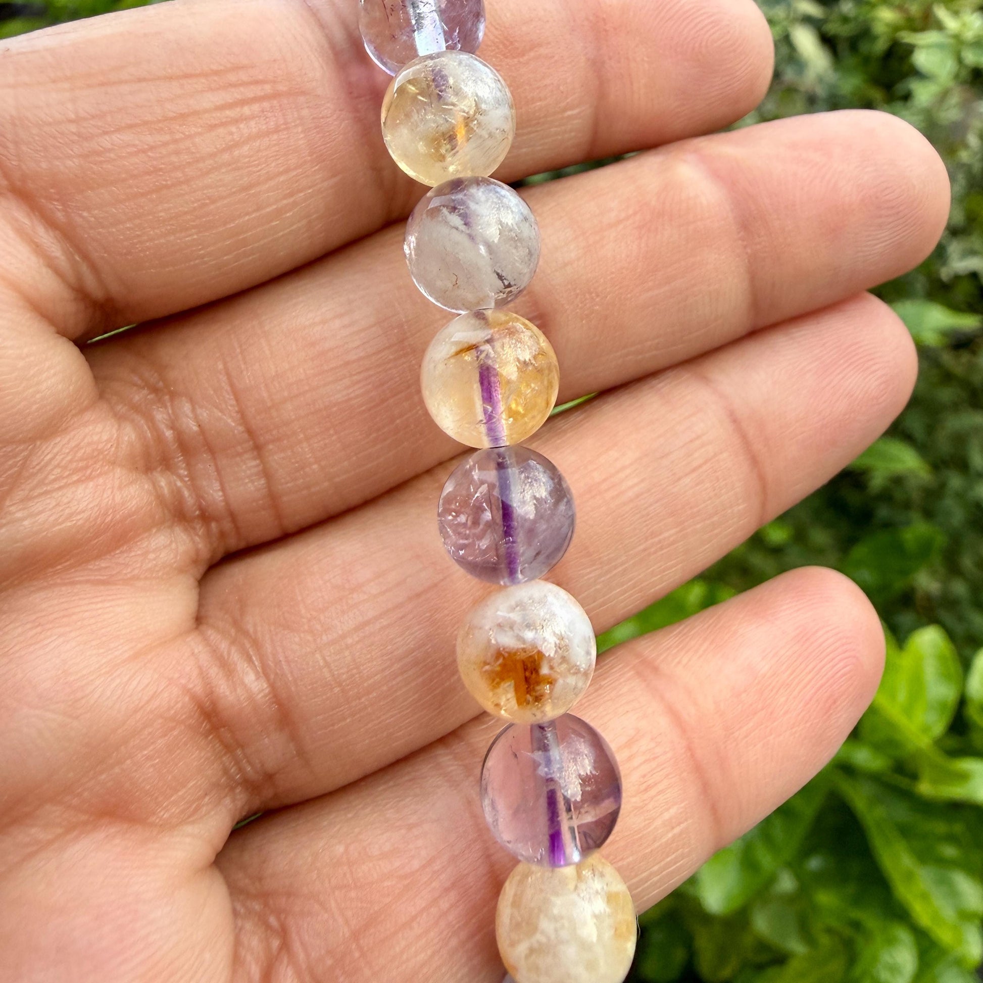 May include: A strand of spherical beads featuring a mix of translucent purple amethyst and golden yellow citrine. Each bead displays natural internal inclusions, varying color gradients, and a polished, smooth surface texture throughout.