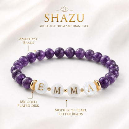 May include: A beaded bracelet featuring round purple amethyst beads, gold-toned metal spacers, and four white mother-of-pearl letter beads spelling EMMA in gold font. The design includes 18K gold plated disks and small gold-toned accent beads.