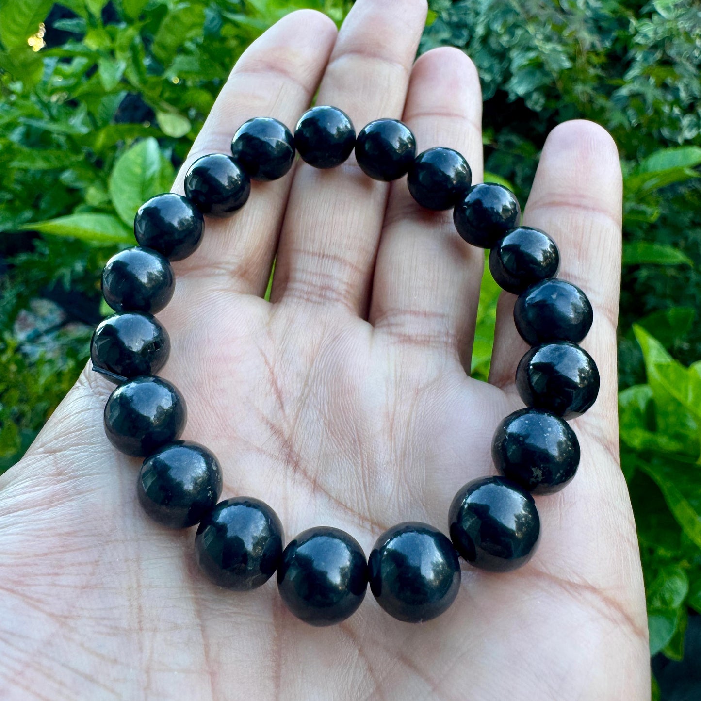 May include: A circular stretch bracelet composed of smooth, polished, spherical black beads. The beads are uniform in size and arranged in a continuous loop, reflecting light on their glossy surfaces, creating a dark, monochromatic appearance.