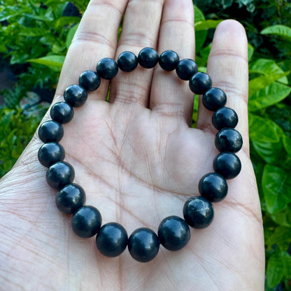 May include: A circular stretch bracelet composed of smooth, round, dark charcoal-gray beads. The beads have a subtle, polished sheen and are uniform in size, strung together to form a continuous loop that rests against the palm of a hand.
