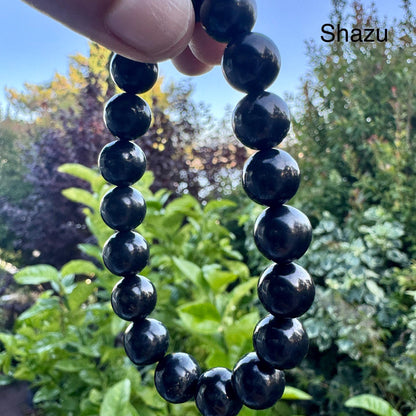 May include: A beaded bracelet featuring smooth, round, polished black beads strung together in a circular loop. The beads have a reflective surface and are uniform in size. The word Shazu is printed in the upper right corner of the image.