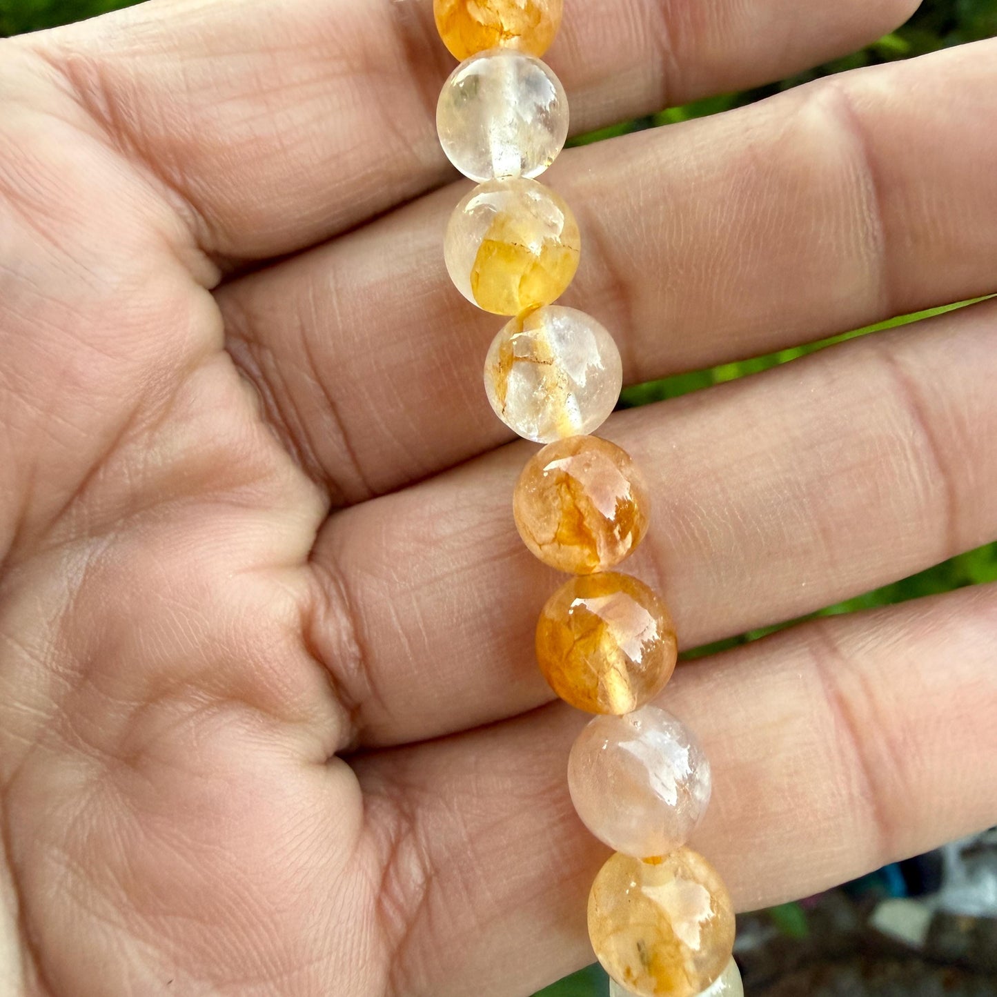 May include: A strand of round, polished beads featuring a mix of translucent clear and vibrant golden-yellow hues. Each bead displays unique internal inclusions and natural variations in color, ranging from pale yellow to deep amber tones.