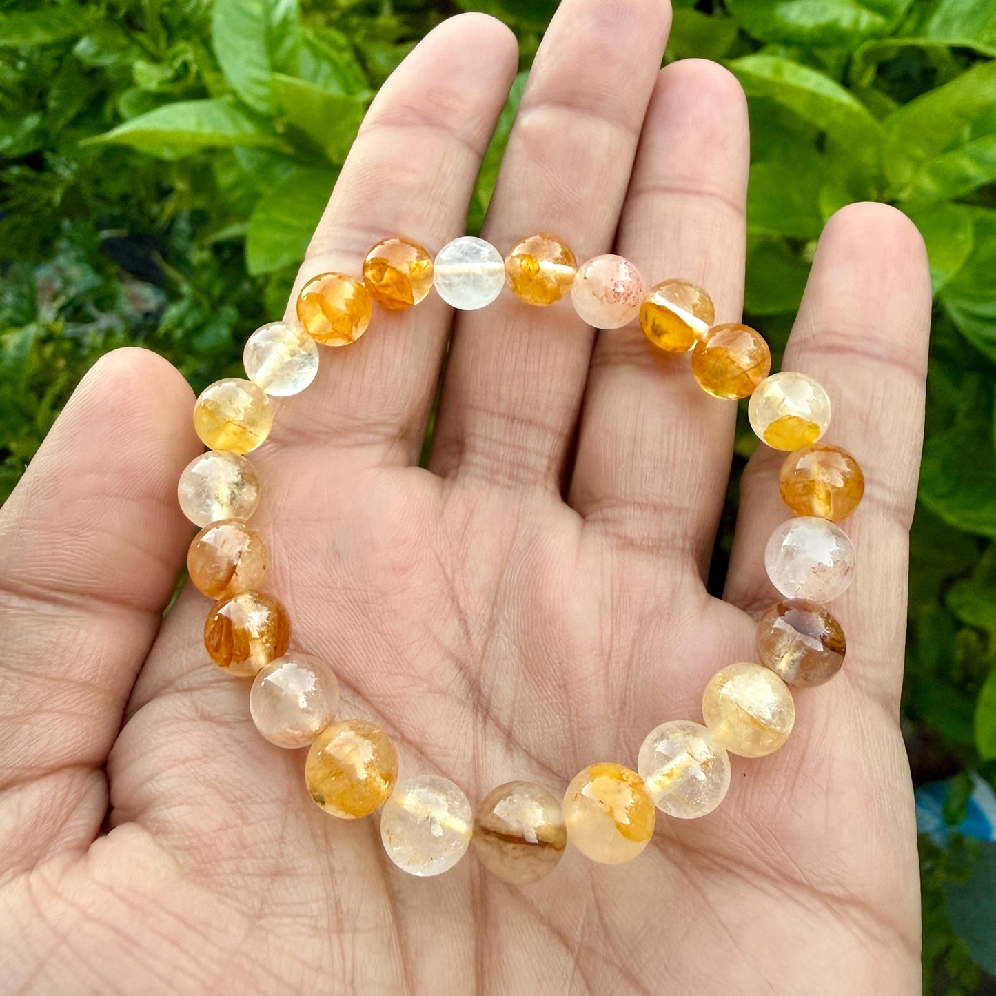 May include: A beaded bracelet composed of round, polished gemstones in varying shades of translucent yellow, orange, and clear white. The beads are strung together in a circular pattern, displaying natural inclusions and variations in color intensity.