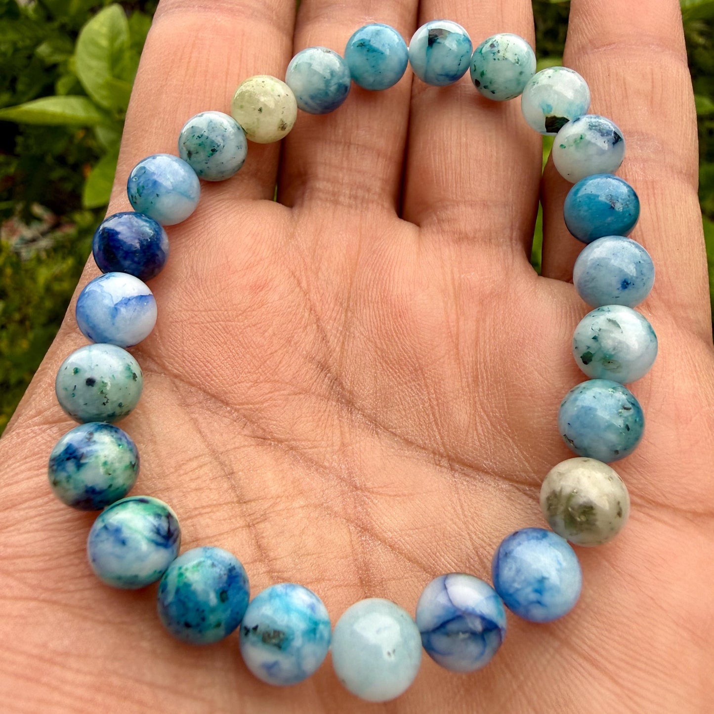 May include: A circular beaded bracelet composed of smooth, polished spherical stones. The beads feature a marbled pattern with varying shades of sky blue, deep navy, and creamy white, creating a variegated appearance throughout the entire piece.