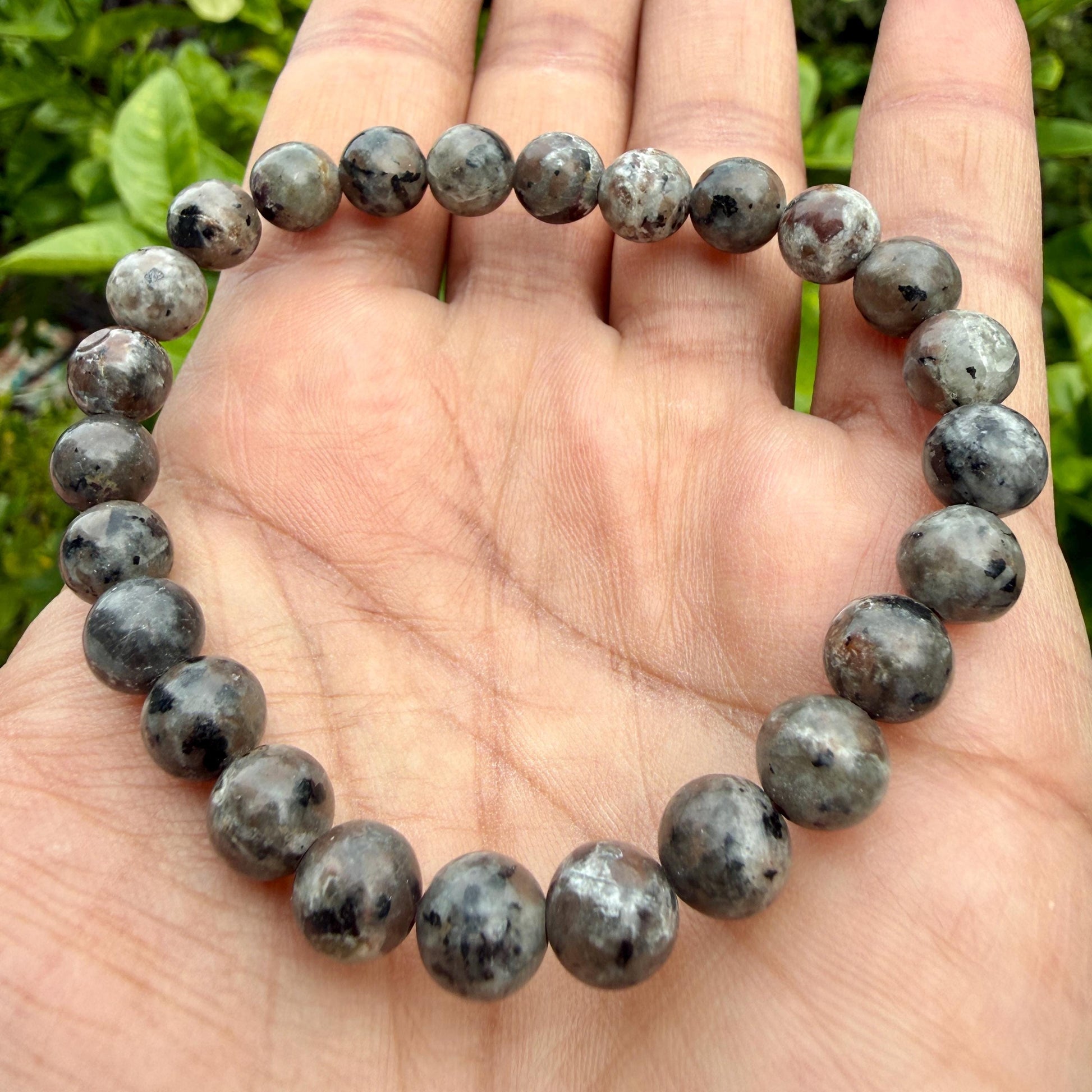 May include: A stretch bracelet composed of round, polished beads in shades of gray, charcoal, and black. The beads feature a mottled, speckled appearance with varying levels of opacity and dark inclusions throughout the circular stone arrangement.