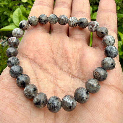 May include: A stretch bracelet composed of round, polished beads in shades of gray, charcoal, and black. The beads feature a mottled, speckled appearance with varying levels of opacity and dark inclusions throughout the circular stone arrangement.