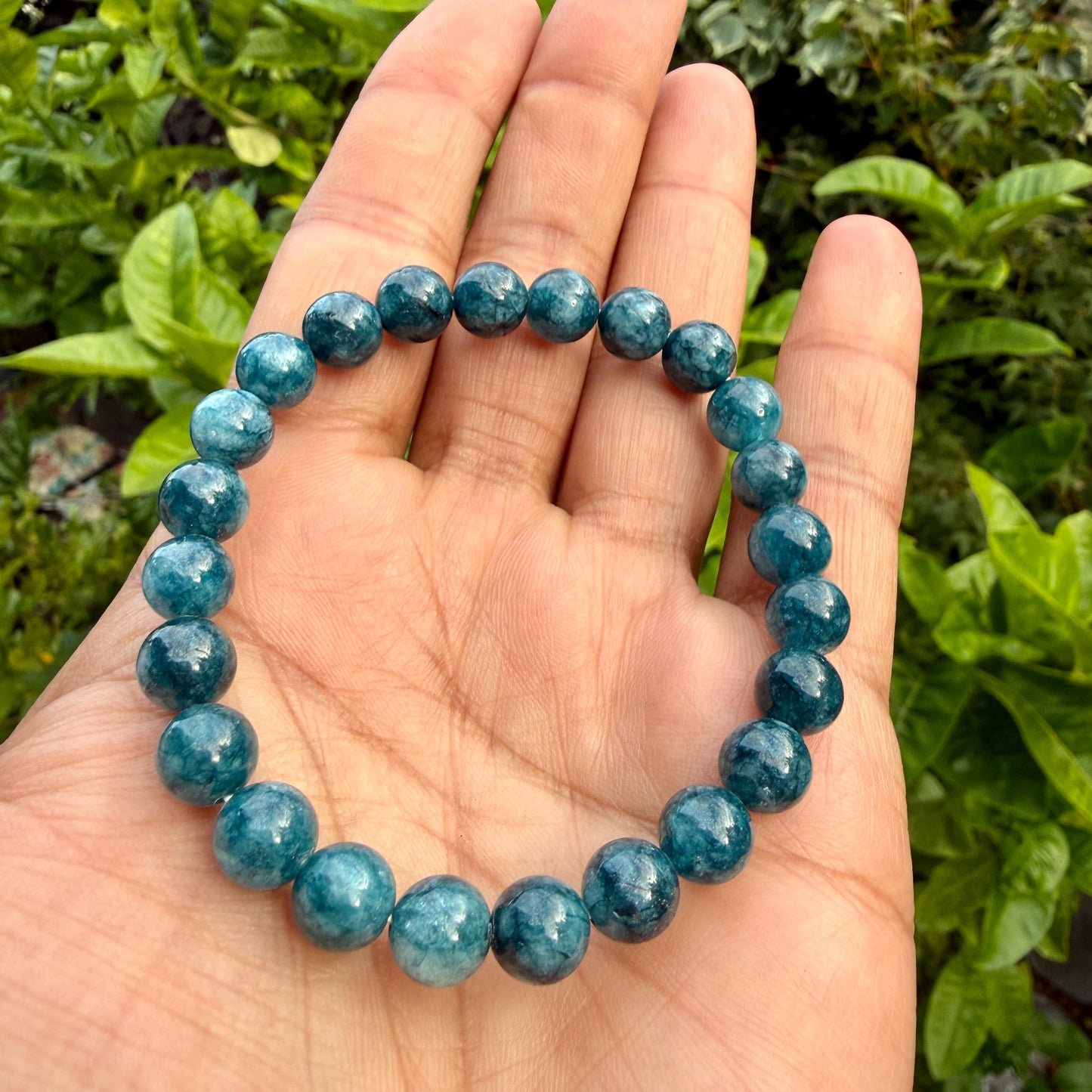 May include: A stretch bracelet composed of round, polished blue apatite beads. The beads exhibit varying shades of deep teal and ocean blue with natural internal inclusions and a smooth, glossy finish, strung together on a flexible elastic cord.