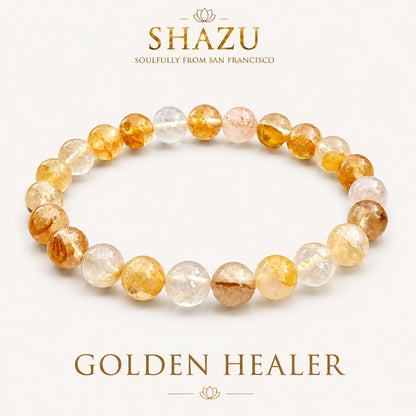May include: A circular bracelet composed of round, translucent beads in varying shades of yellow, gold, and clear white. The text SHAZU SOULFULLY FROM SAN FRANCISCO and GOLDEN HEALER appears above and below the jewelry piece on a plain background.